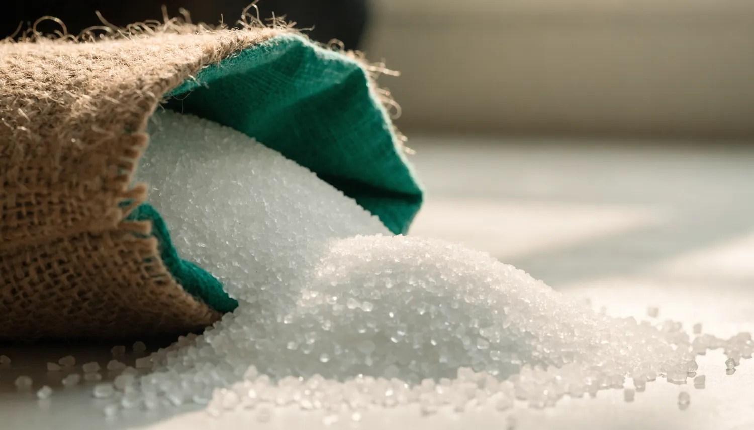Refined white sugar crystals beside a burlap sack